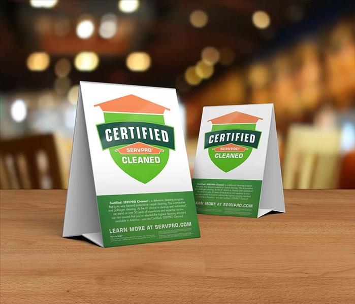 Table tent signs describing the Certified: SERVPRO Cleaned program on top of a wooden table.